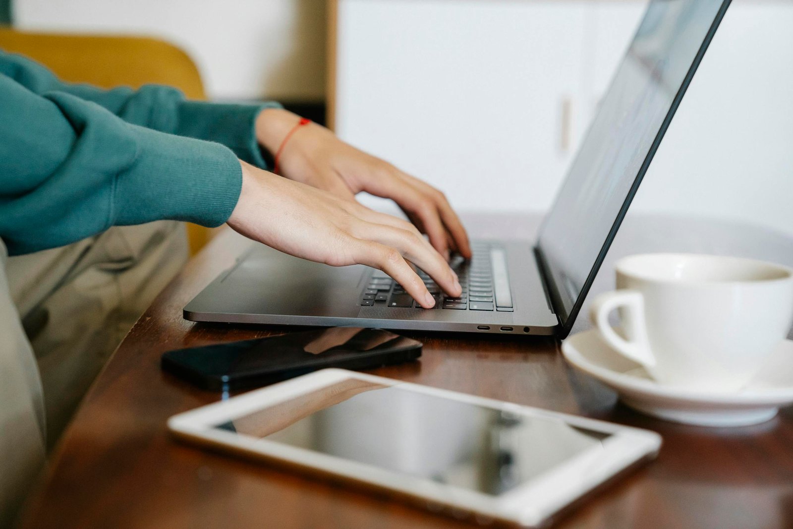 Side view of crop anonymous male remote worker browsing netbook while sitting at table with cup of coffee smartphone and tablet